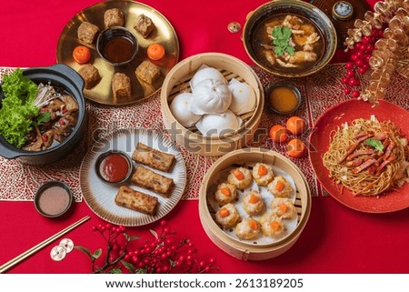 A complete set of dim sum dishes including noodles, dumplings, buns and vegetables on festive red table.