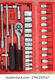 Complete socket wrench set neatly organized in a red plastic case. Includes ratchet handle, extension bars, metric sockets, and screwdriver bits. Polished steel finish, essential tool kit for repairs and assembly work.