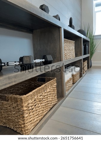 A complete view down the side of a gym shelf lined with weights, towels, and baskets. Light streaming in from the window adds warmth.