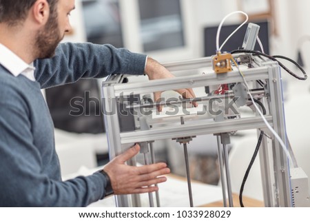Complete work. Dark-haired bearded young engineer removing a recently printed 3D model from the printer with one hand while holding onto the body of the device with the other hand