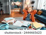 Completed homework. Relaxed little girl in home clothes leaning on back of chair with hands behind head and closed eyes. Calm kid finishing daily self studying by desk with coloured stationery.