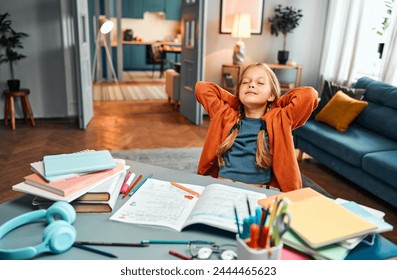 Completed homework. Relaxed little girl in home clothes leaning on back of chair with hands behind head and closed eyes. Calm kid finishing daily self studying by desk with coloured stationery. - Powered by Shutterstock