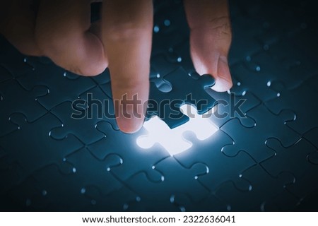 Completing blue jigsaw puzzles with the last piece on light leaked hole gap in dark room by hand background. Business success strategic solutions and problem solving challenge concept.