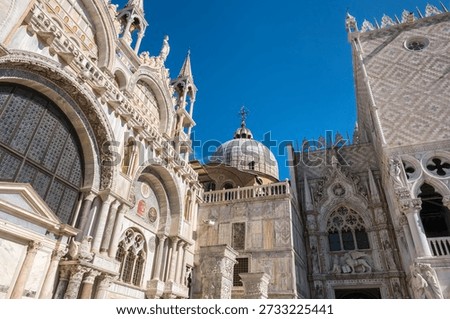 The complex architectural connection between Saint Marks Basilica and the Doges Palace, Venice, Italy showing marble carvings, arches, and a dome against a bright blue sky.