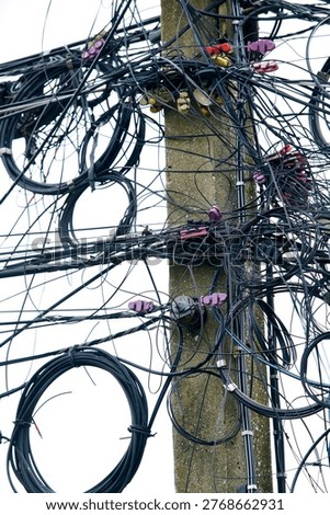A complex arrangement of wires and cables wraps around a utility pole against a clear sky, showcasing the intricacies of urban infrastructure and electrical connections.