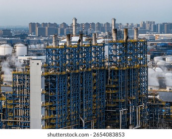 Complex blue steel frame structure of a chemical plant with a city skyline in the background
