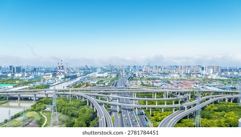 Complex elevated interchange spans green corridors and a river; red-and-white industrial chimneys and dense urban skyline visible under bright blue sky, Nantong city, Jiangsu province, China