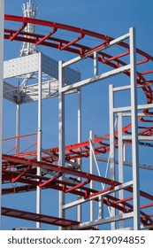 the complex geometry of a roller coaster's red tracks and white steel support beams against a clear blue sky.