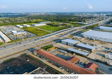Complex multi level highway intersection with industrial warehouses, parking lots, surrounding suburban landscape in Houston, Harris County, Texas.