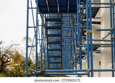 A complex network of blue scaffolding is set up against building construction, with white domed structure visible background. scene captures intricate geometry and industrial feel of construction