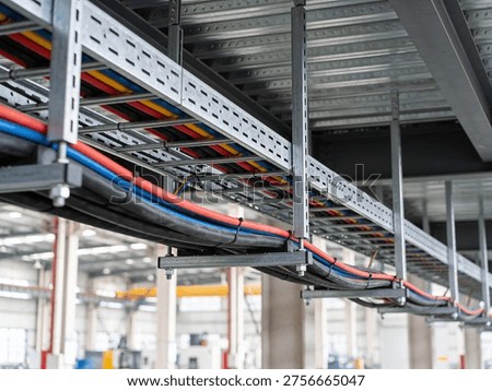 A complex network of electrical cables and conduits suspended from the ceiling in a factory setting, showcasing organized infrastructure