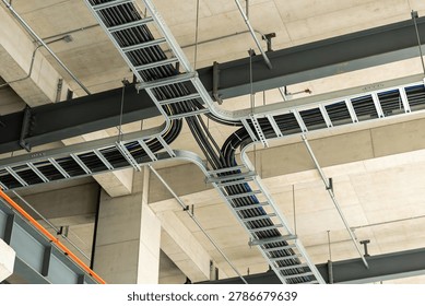 A complex network of electrical conduits and cable trays is neatly organized and suspended from a concrete ceiling structure
