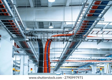 A complex network of overhead cable trays and conduits neatly routes electrical wires and data cables throughout a large industrial building