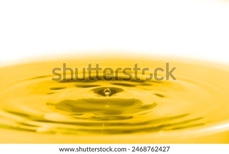 A complex pattern of concentric ripples created by a droplet of oil falling onto the surface of a viscous liquid under the effects of golden lighting and set against white  background for effect.