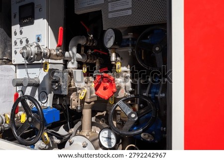 Complex pump control panel inside a fire truck showing valves, pressure gauges, hoses, levers and connectors used to control and monitor water flow and pressure during firefighting operations.
