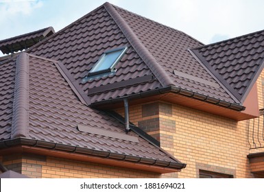 Complex roof design, metal tiled expensive roofing construction with a skylight, snow guards, chimney of a brick house.