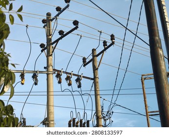 A complex web of electrical power lines crisscrosses between multiple utility poles, showcasing the infrastructure for electricity distribution under a bright, clear blue sky.