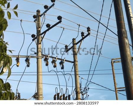 A complex web of electrical power lines crisscrosses between multiple utility poles, showcasing the infrastructure for electricity distribution under a bright, clear blue sky.
