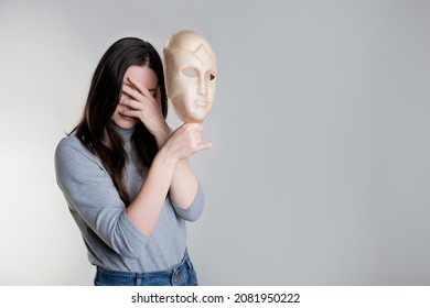 Complexes due to appearance or self-identification problems, concept. A young woman holds a mask in her hands hiding her face. Photos in light gray tones, gray background - Shutterstock ID 2081950222