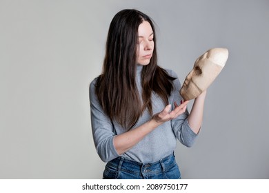 Complexes due to appearance or self-identification problems, concept. A young woman holds a mask in her hands hiding her face. Photos in light gray tones, gray background