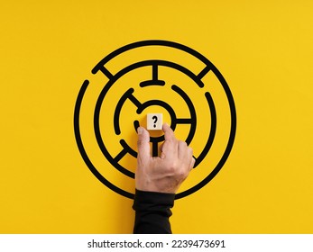 Complication, mystery and problem solving. Uncertainty and challenge in business. Hand puts a wooden cube with question mark symbol in the middle of a maze. - Powered by Shutterstock