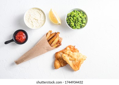 Components Of Traditional British Set Of Fish And Chips Beer Battered Cod Fillet, Fries , Lemon Slices, Tartar Sauce And Mushy Peas , Tomato Ketcup For Choice Over White Concrete Background Top View