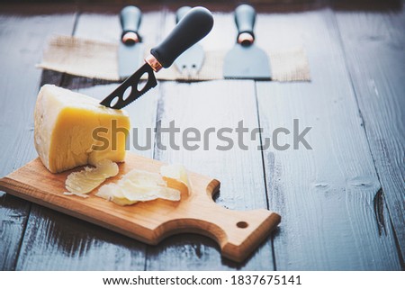 Composed cloesup detail view of aged cheddar cheese with cheese knife set, over vintage brown wooden backdrop