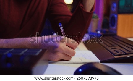 Composer developing an original track In his home studio, writing down lyrics and harmonic notes before recording the song melody. Musician using DAW computer apps for creating music. Camera B.