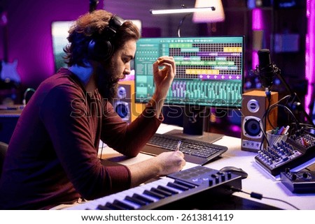 Composer songwriter taking notes to create a new song in his home studio, writing down lyrics and musical notes before recording his tune on mixing console and microphone, music industry.