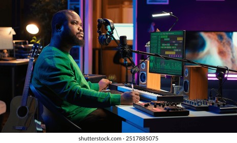 Composer writes verses and ideas to develop original song in home studio before recording new audio files. Songwriter using musical equipment and his imagination, artist composes music. Camera A.