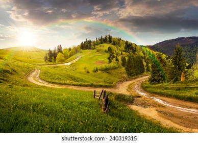 composite autumn landscape. fence near the cross road on hillside meadow in mountains. few fir trees of forest  on both sides of the road in sunset light with rainbow