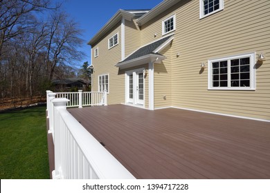 Composite Deck In House Backyard. Brown Boards, White Railing Posts And Veranda. Large, Spacious, New Construction.