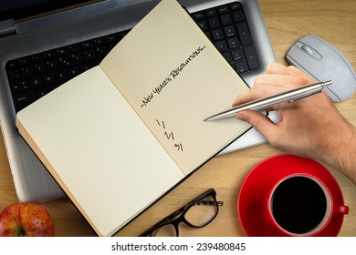 Composite Image Of Hand Writing New Years Resolutions Against Overhead Of Laptop With Notebook