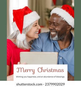 Composite of merry christmas text over diverse smiling couple in santa hats using tablet. Wishing you happiness and an abundance of blessings, together, love, festivity, winter holiday, celebrate. - Powered by Shutterstock