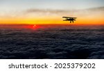 Composite of the silhouette of a bi-plane flying above the clouds at sunset