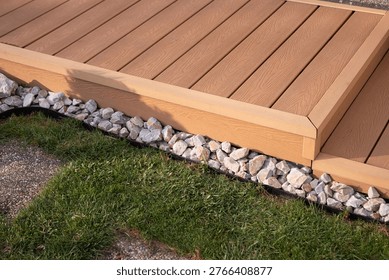 Composite WPC terrace decking with step and corner trim, garden walkway detail with grass and decorative stones, close-up.