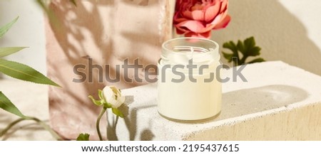 Composition with aromatic candle in jar on concrete podium. Mockup soy wax candle in natural style with flower. Scented handmade candle with wick.  Handmade spa product  from soy wax in glass
