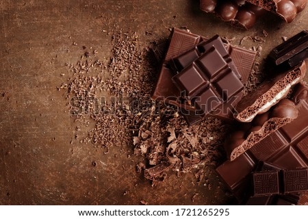 Composition of bars and pieces of different milk and dark chocolate, grated cocoa on a brown background top view close up