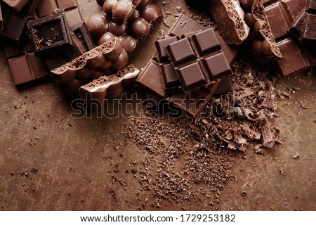Composition of bars and pieces of different milk and dark chocolate, grated cocoa on a brown background top view close up