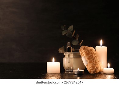 Composition with bath sponge, bottle of cosmetic product and burning candles on black background, closeup