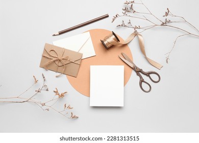 Composition with blank card, envelopes, scissors, ribbon and dried flowers on white background