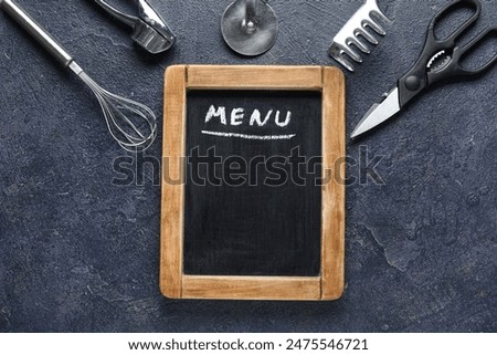Composition with blank menu board and kitchen utensils on dark background