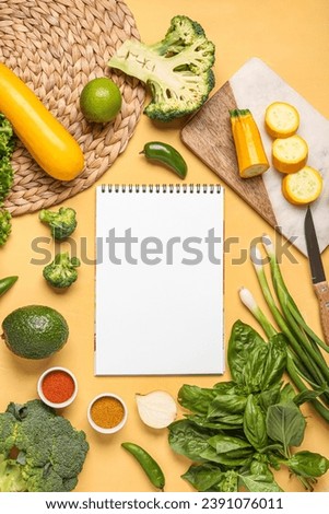Composition with blank recipe book, fresh vegetables and spices on yellow background
