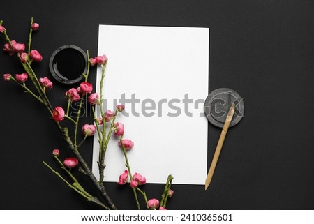 Composition with blank sheet of paper, ink, nib pen and blooming branch on dark background. International Haiku Poetry Day