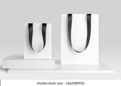 Composition of blank shopping bags mockup with ribbon hangers to place your design. Front view on white background. Fashion branding scene.