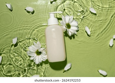 Composición con botella de gel de ducha y flores de manzanilla en agua sobre fondo de color