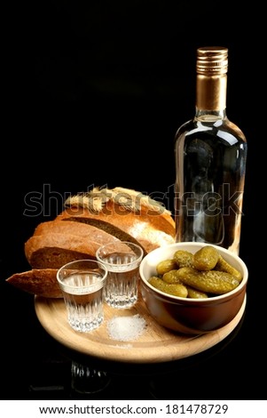 Composition with bottle of vodka, glasses, and marinated vegetables on wooden board, isolated on black