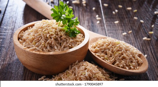Composition with bowl of brown rice on wooden table.