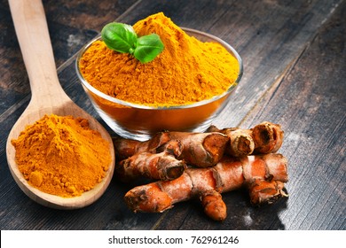 Composition with bowl of turmeric powder on wooden table.