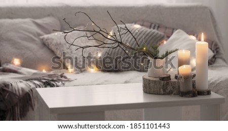 Composition of candles on  white table against the background of  sofa with plaids and pillows. Cozy home concept